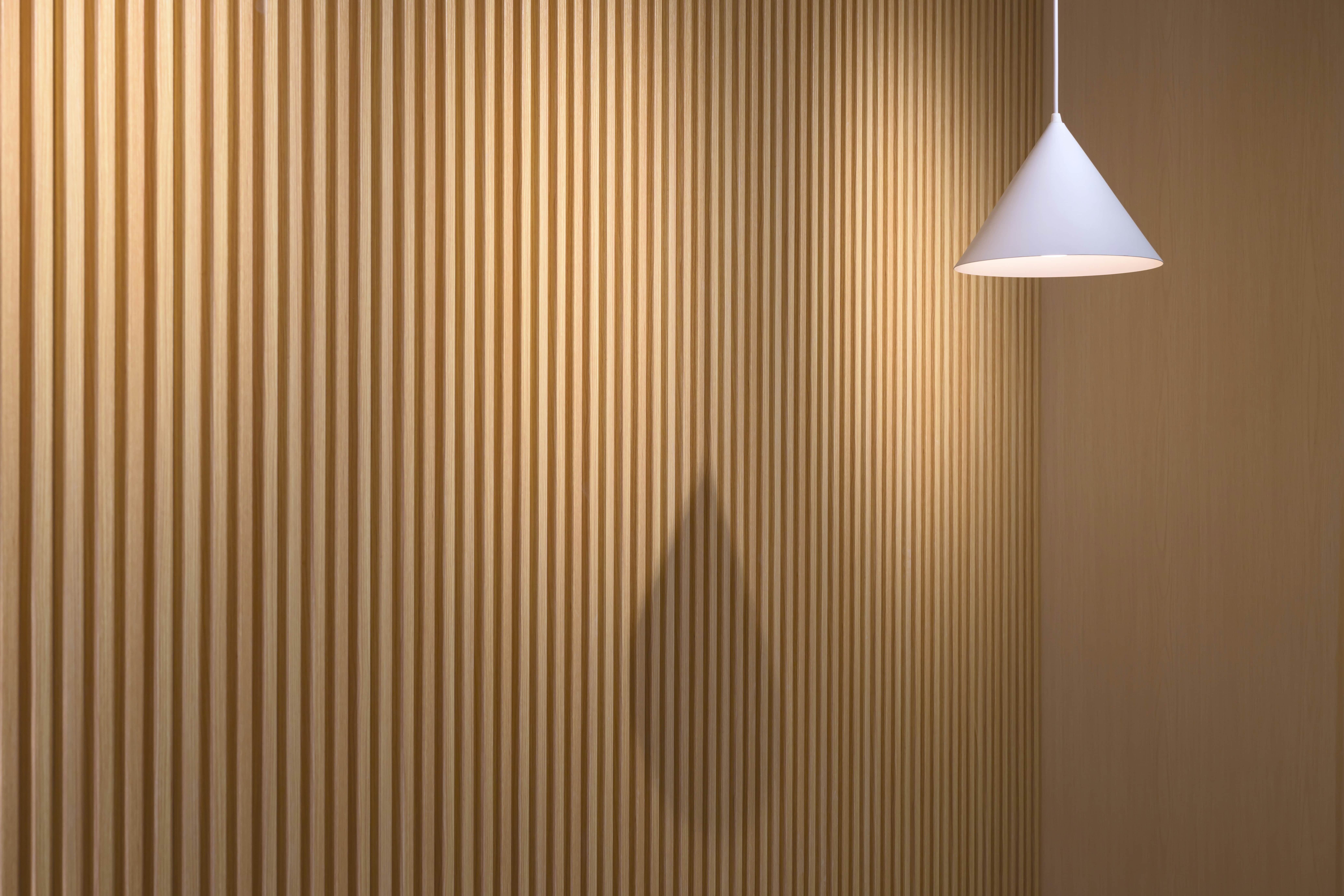 Foto von einer Holzwand mit Lamellen und einer Lampe davor.